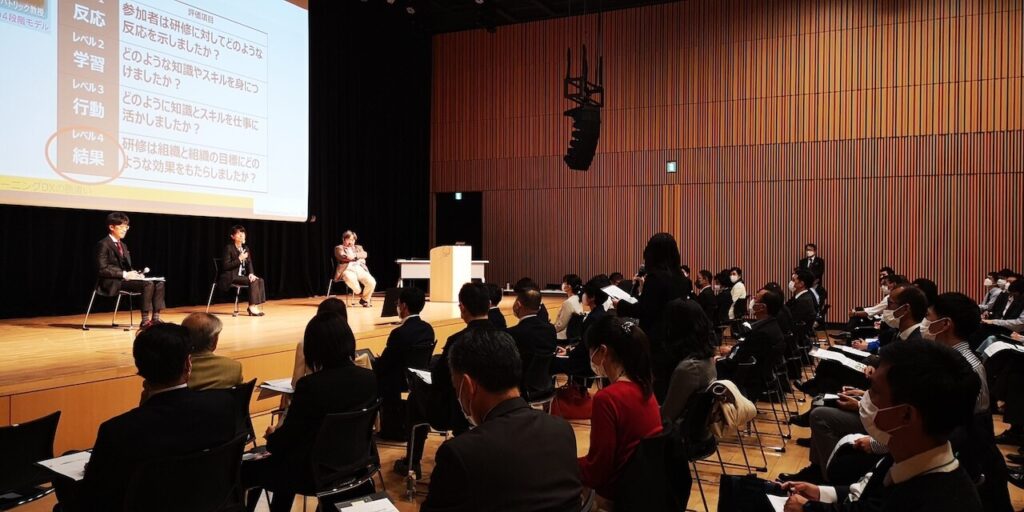 カンファレンス参加者の女性がマイクを持ち、登壇者に質問をしています。